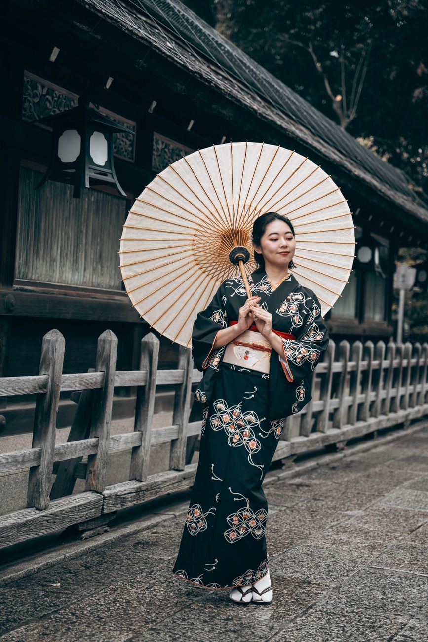 Elegant Japanese woman in traditional kimono walking with paper umbrella in historic Kyoto street.
