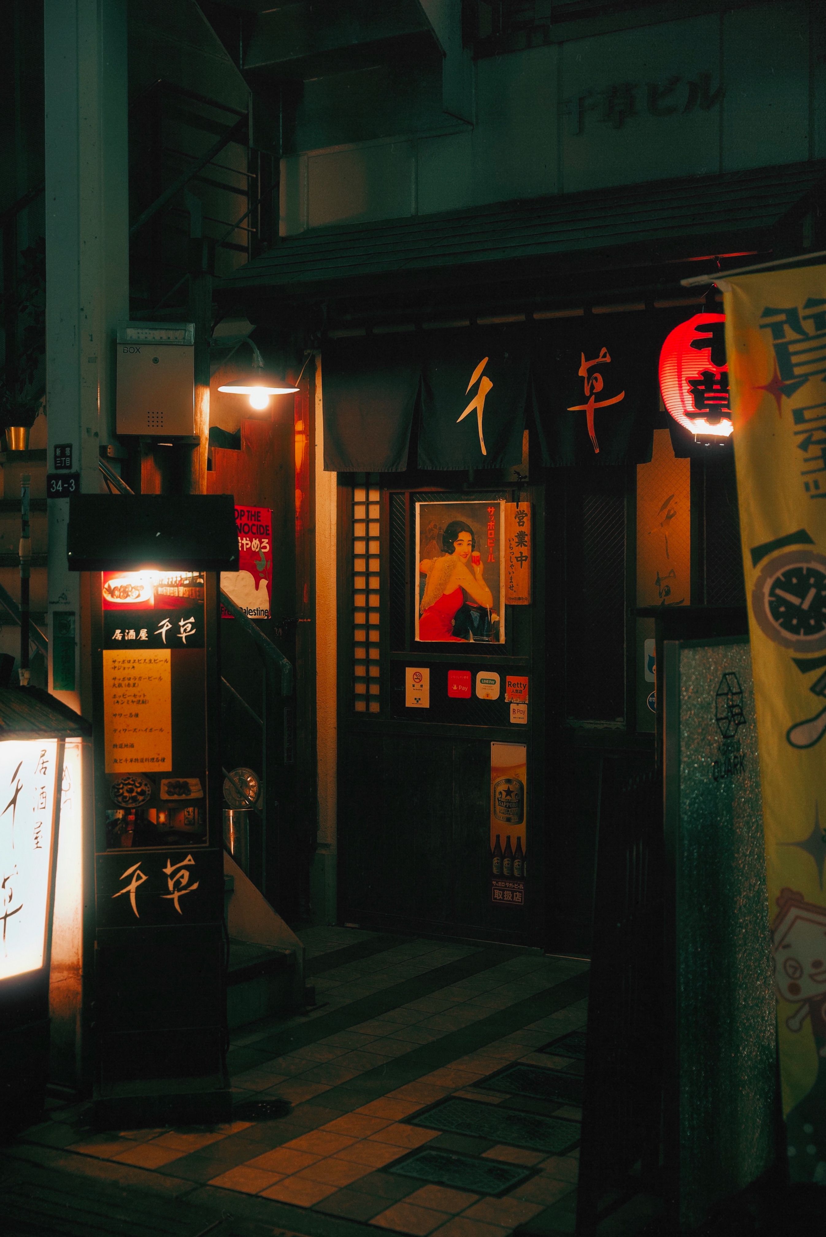 A warm and inviting entrance to a Japanese izakaya at night, adorned with traditional decor and soft glowing lights.
