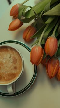 A cozy setup with a cup of coffee and fresh orange tulips on a minimalist white table.