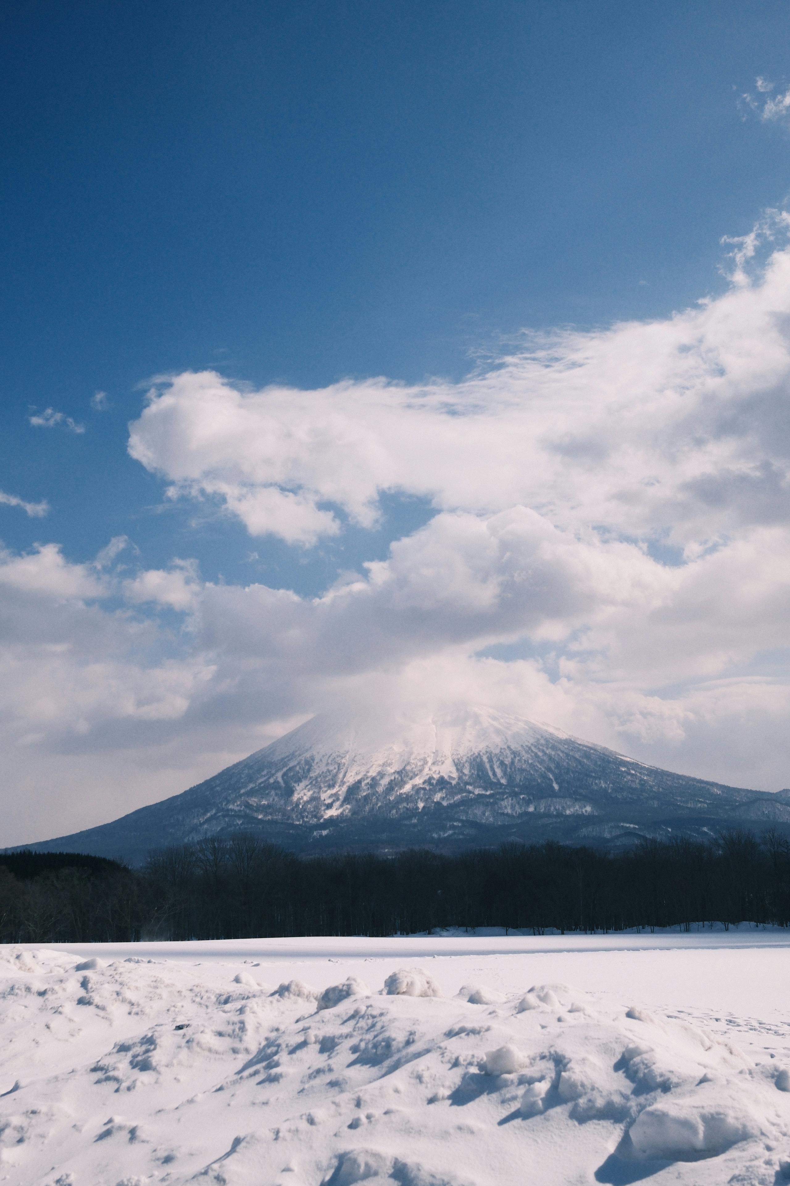 Majestic view of Mt. Yotei in Hokkaido with snow and dramatic clouds against a blue sky.