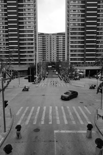 Black and white photo of a city intersection framed by tall symmetrical buildings.