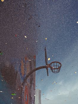 Artistic reflection of a basketball hoop and mural captured on rainy pavement.