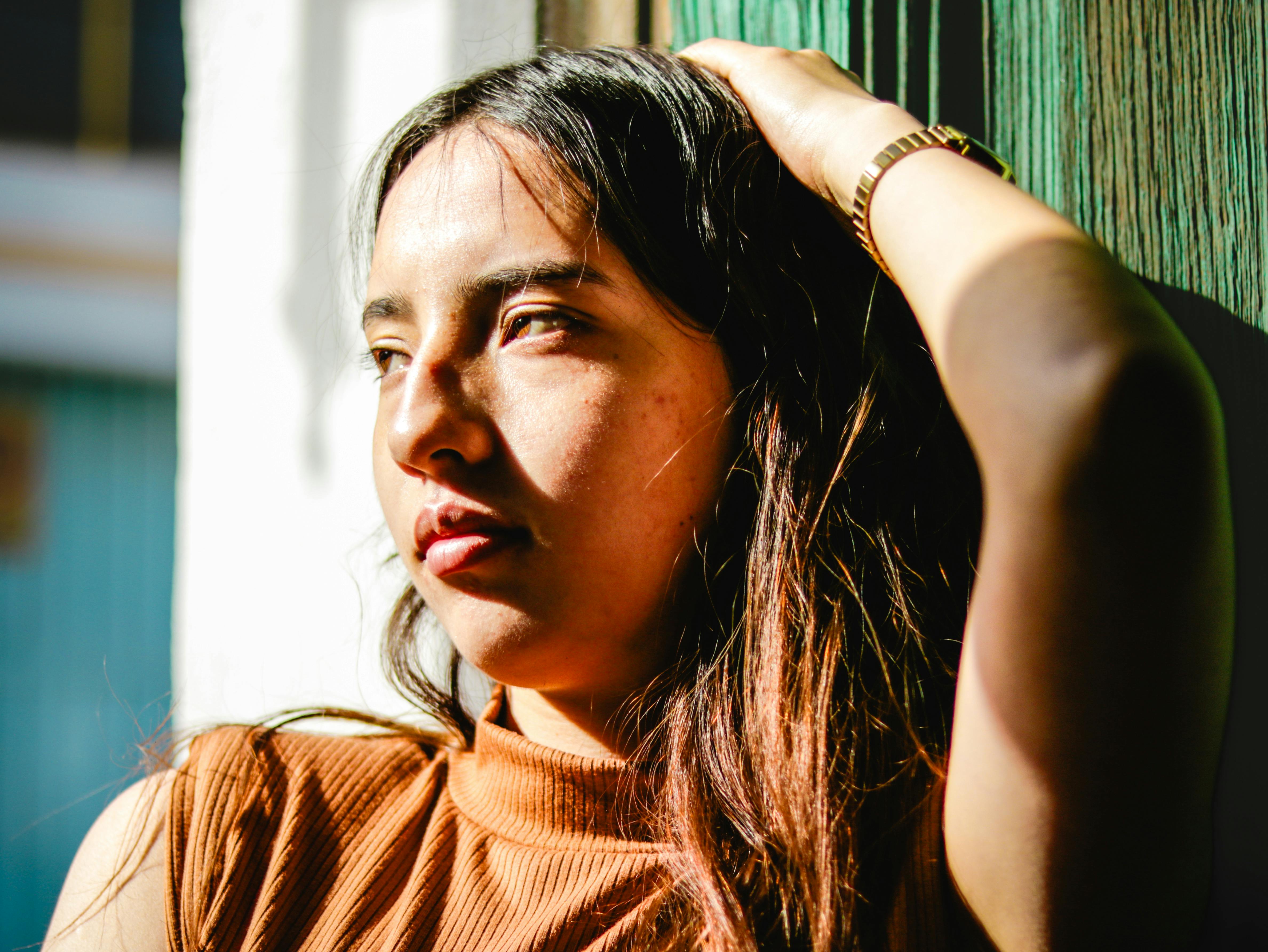 A thoughtful woman gazes out, bathed in warm sunlight, creating a vivid and introspective portrait.