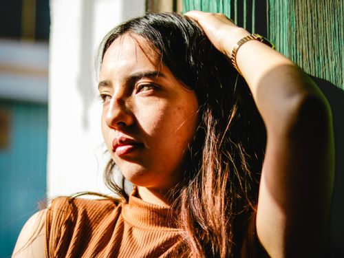 Free A thoughtful woman gazes out, bathed in warm sunlight, creating a vivid and introspective portrait. Stock Photo