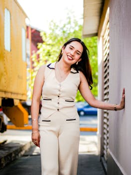 A young woman poses confidently outdoors in elegant beige attire.