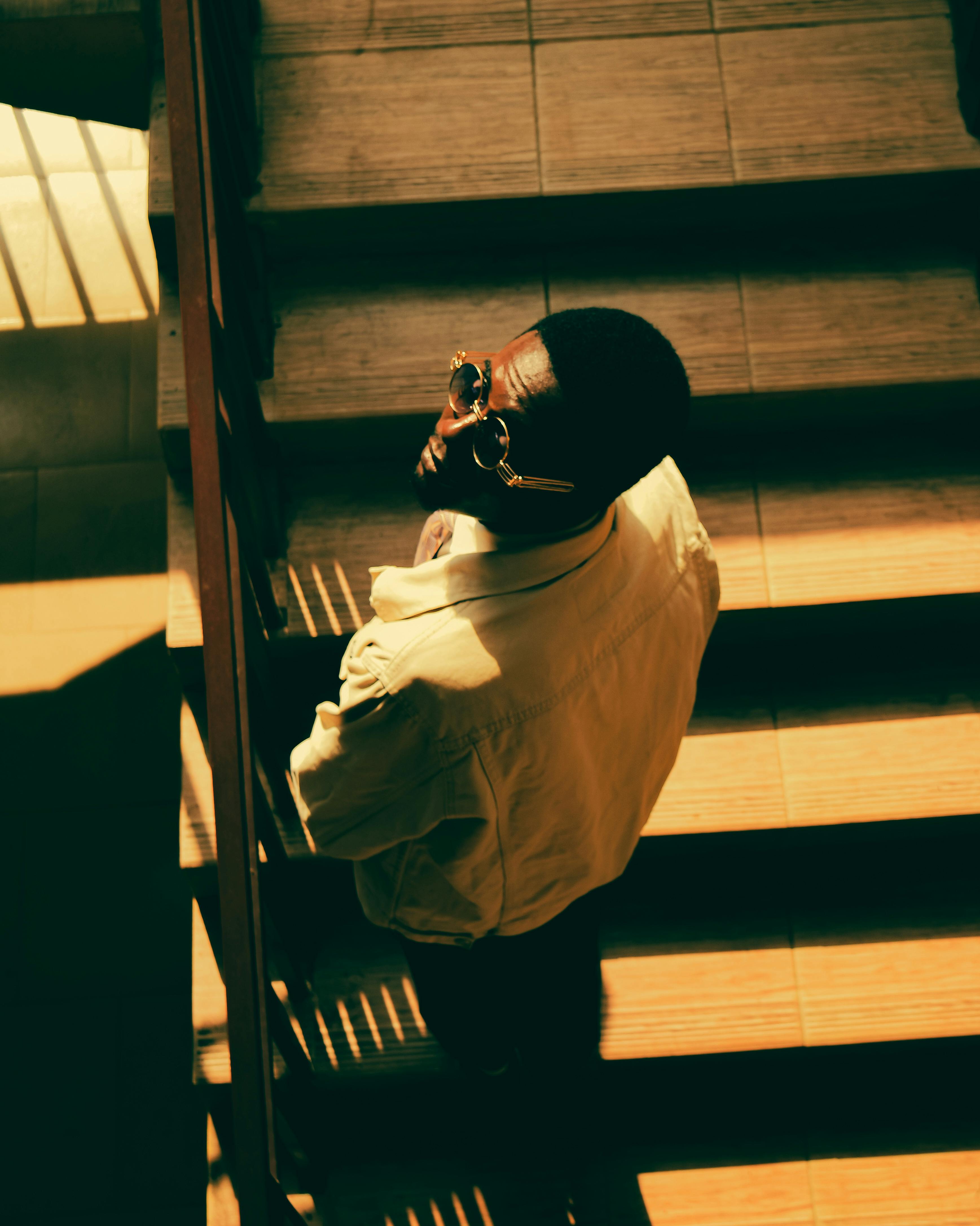 무료 선글라스를 낀 성인 남자가 햇빛이 비치는 실내 계단에 서서 독특한 그림자를 드리우고 있습니다. 스톡 사진