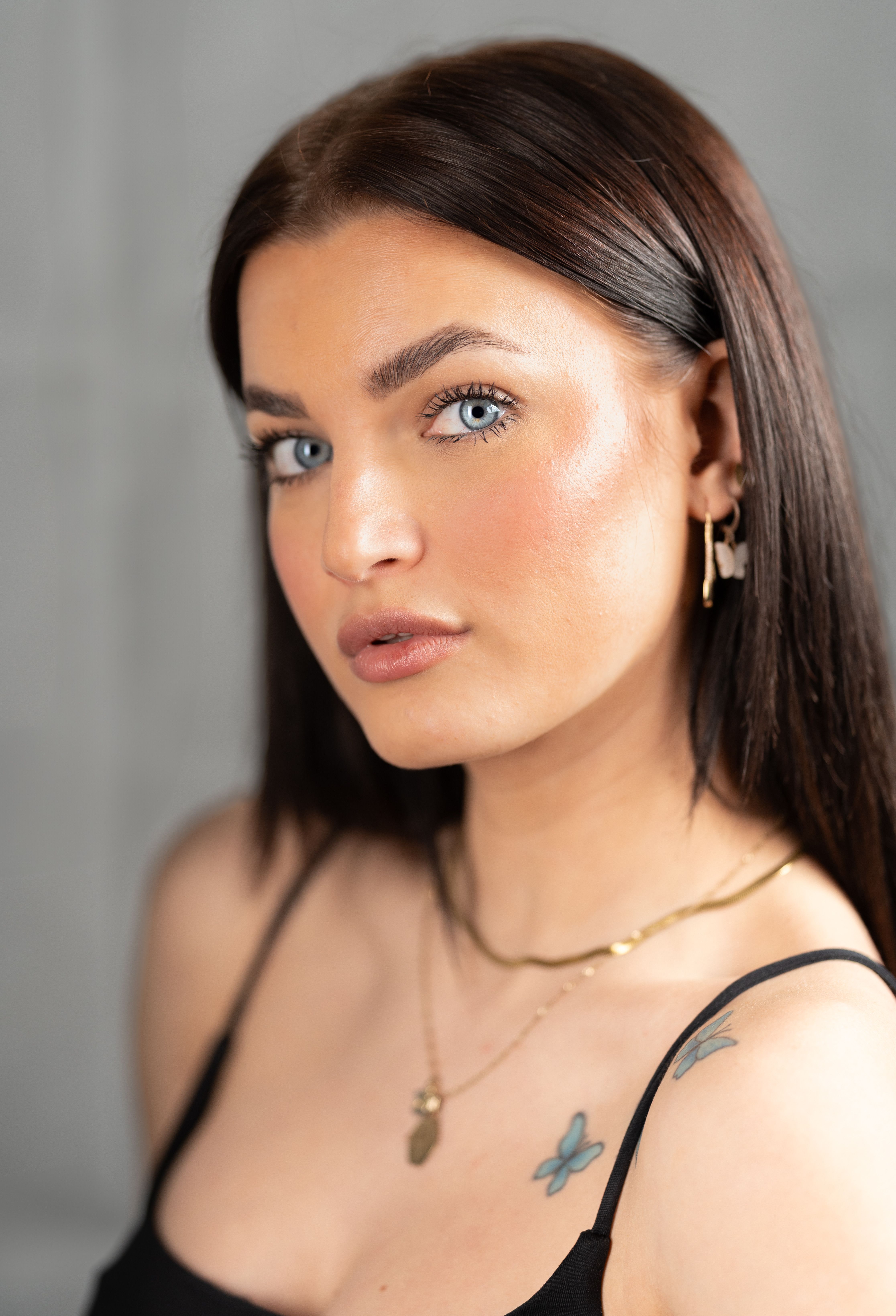 Close-up portrait of a young woman with tattoos, wearing gold jewelry, indoors.