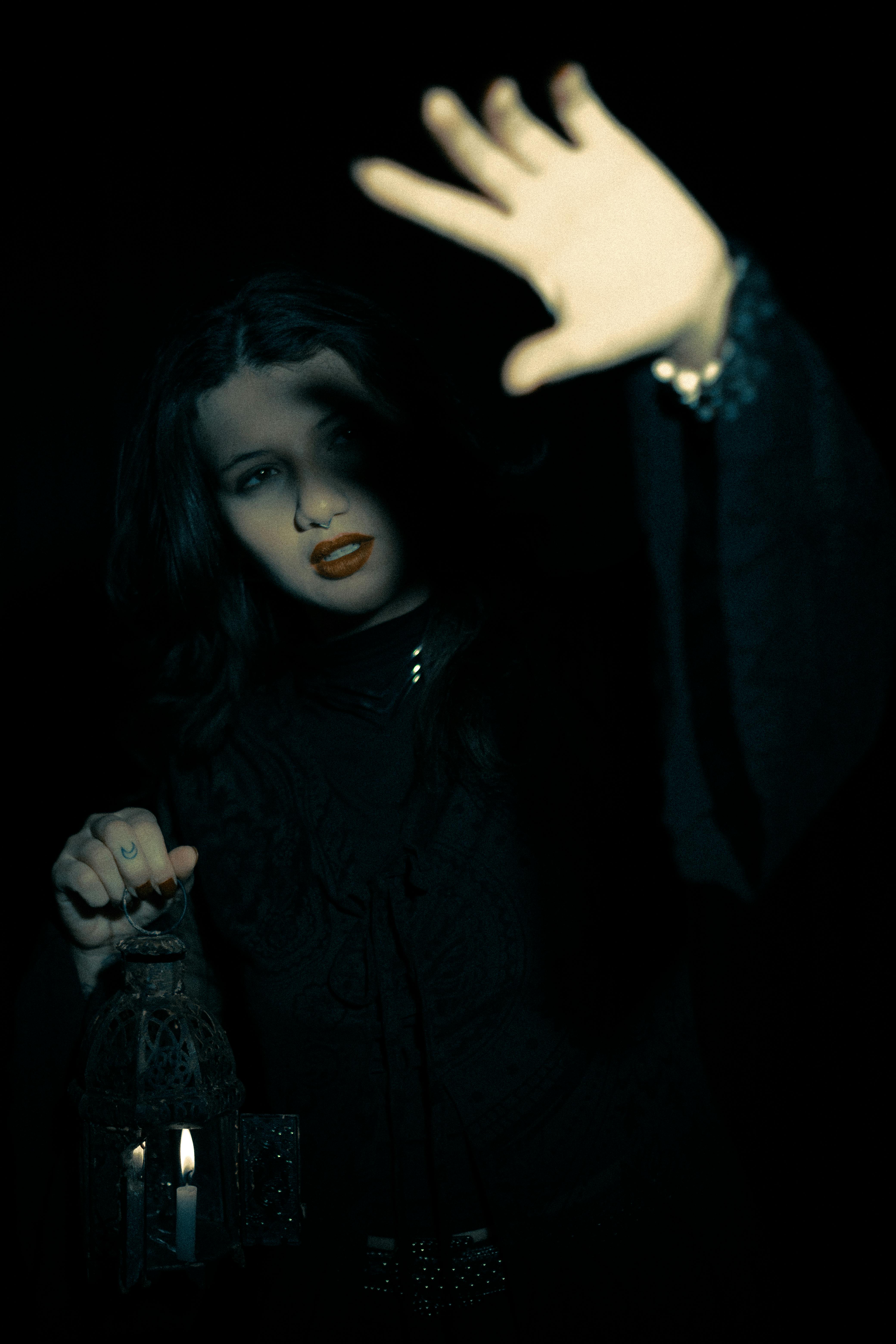 A mysterious woman in dark attire holds a lantern, casting dramatic shadows.