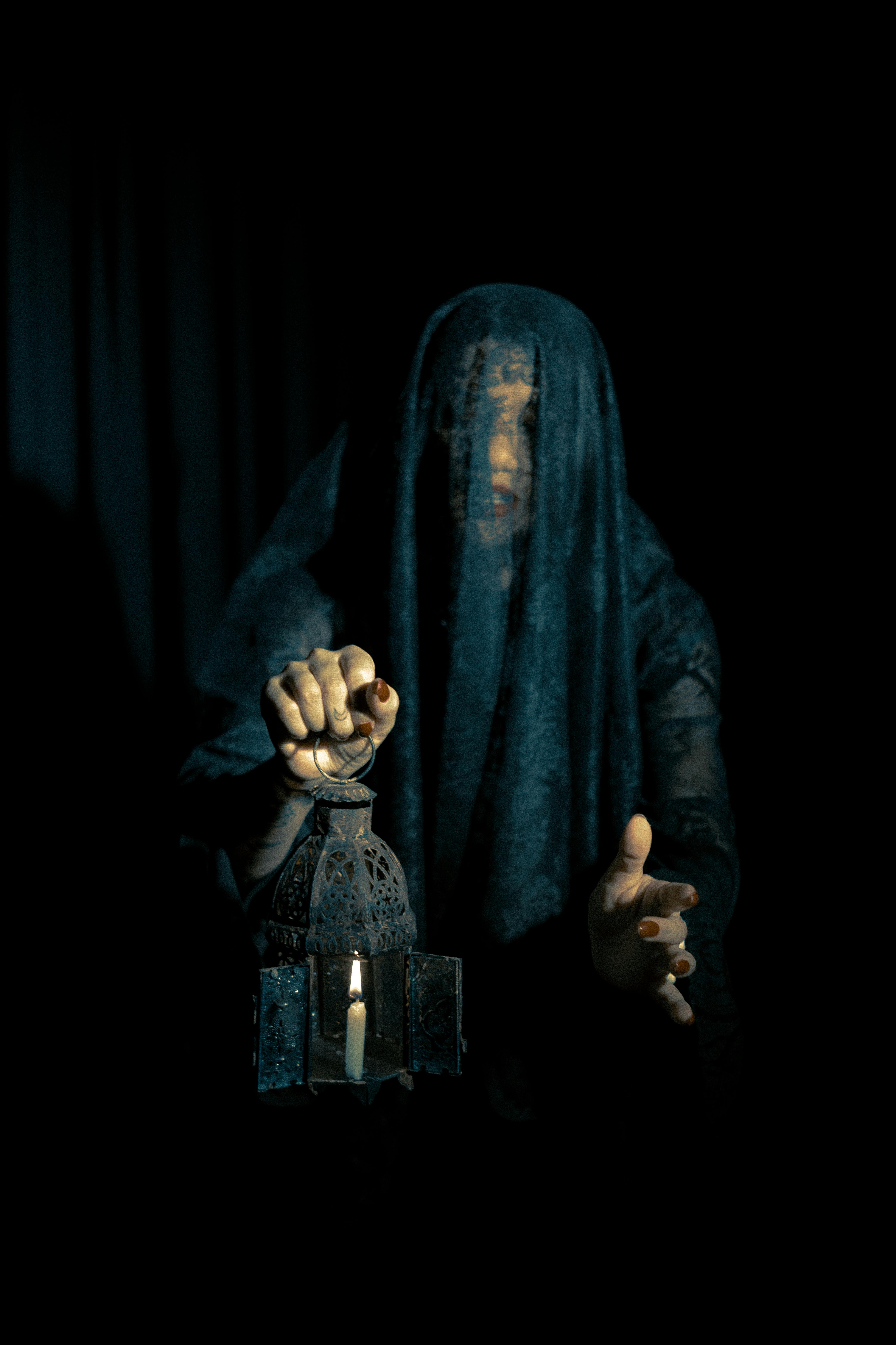 A cloaked figure holds a lit lantern in an enigmatic, dark setting.