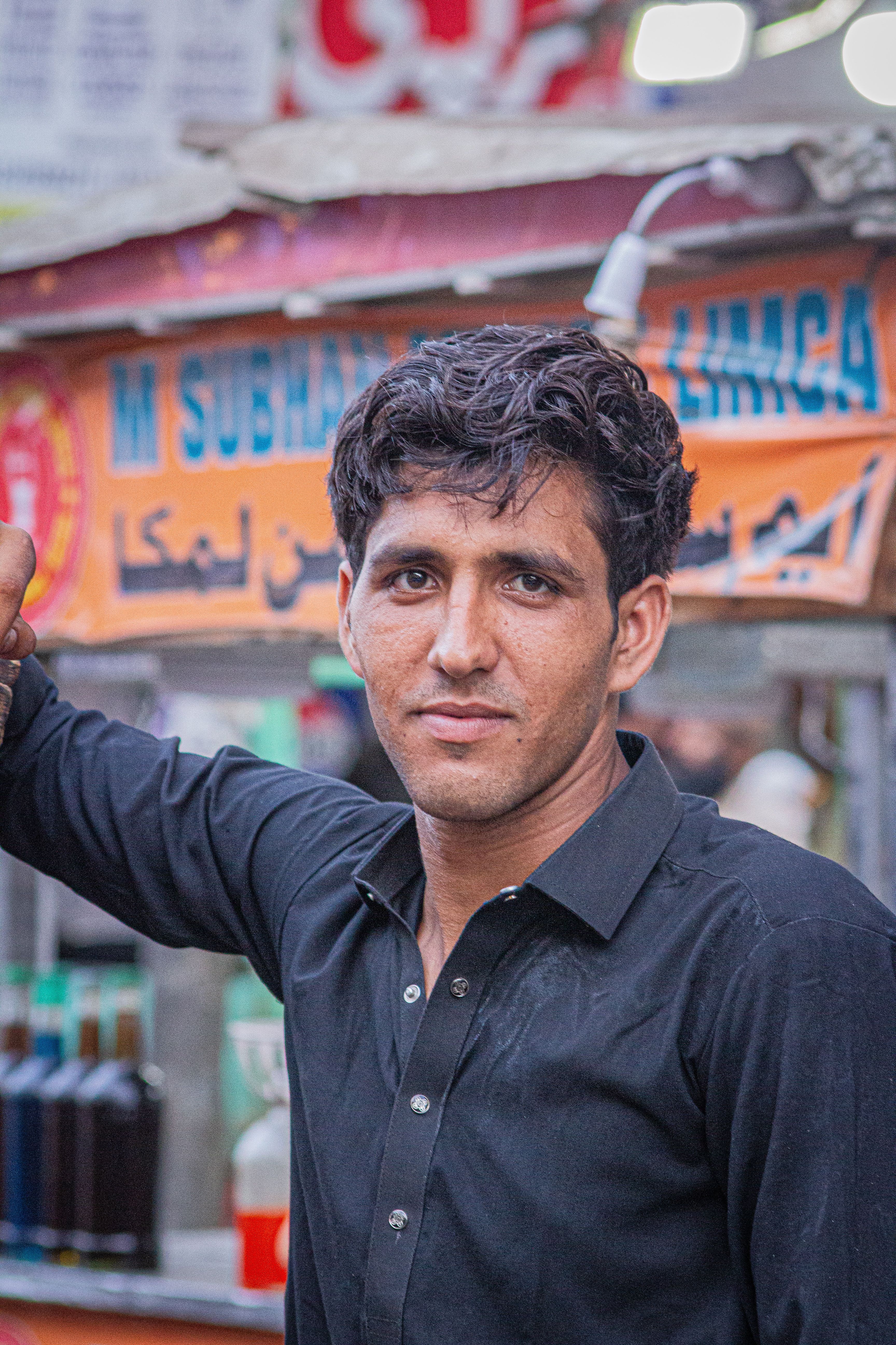 Young man in black shirt poses confidently at a bustling outdoor market.