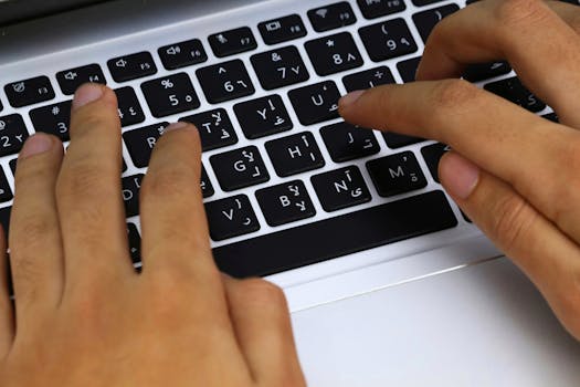Close-up of hands typing on an Arabic layout laptop keyboard, showcasing modern technology in use.