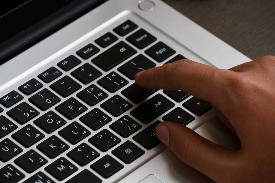 アラビア文字が書かれたノートパソコンのキーボードで入力している手のクローズアップ画像。モダンなワークスペースのセットアップ。