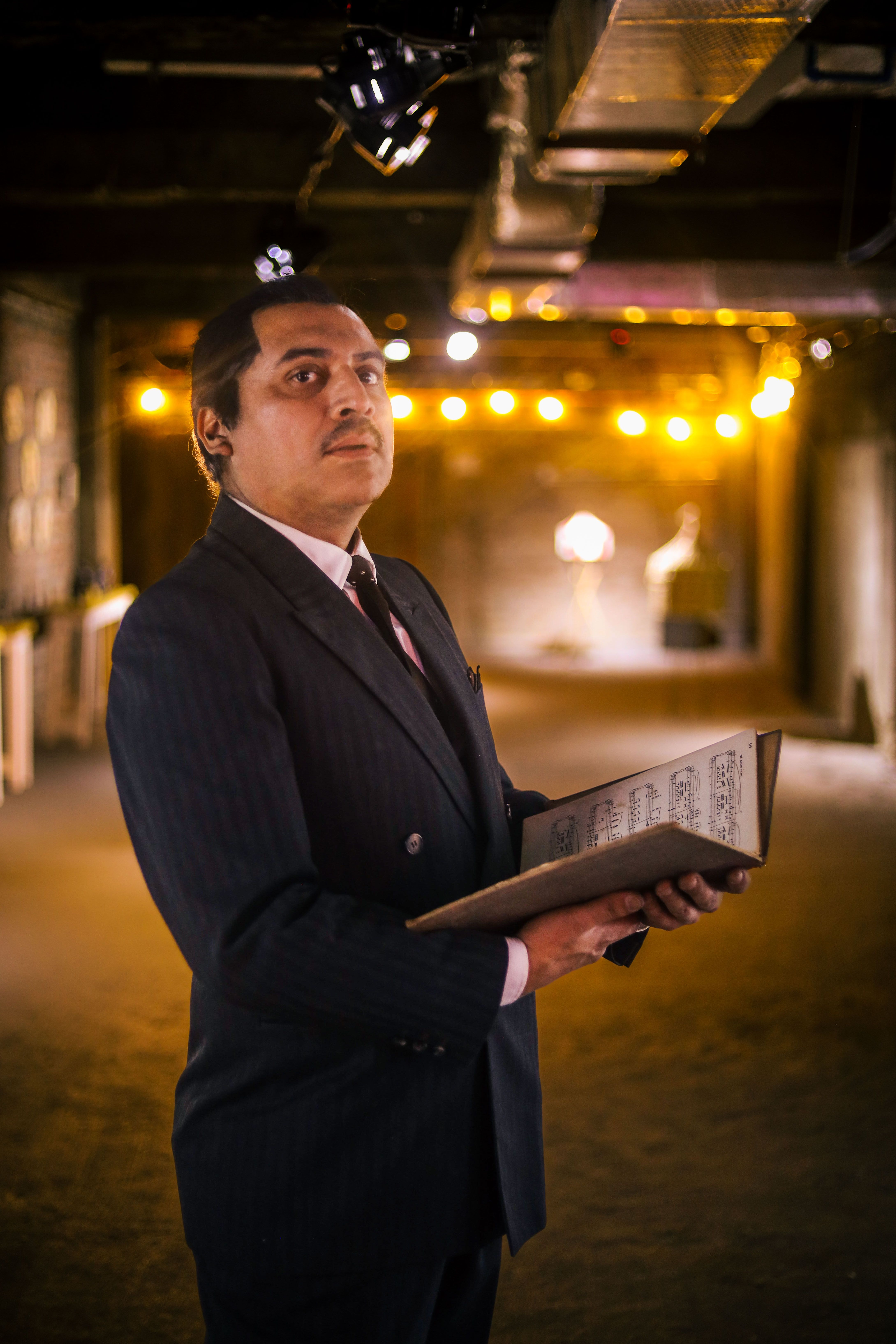Man in vintage suit holding book in dimly lit room with warm lighting.