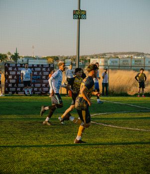 Players compete in an intense amateur soccer match under clear skies on a lush green field.