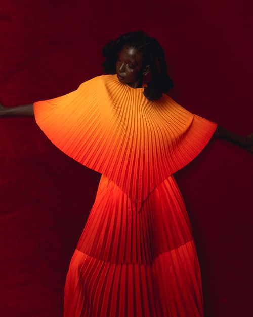 Free Striking image of a woman in a vivid red and orange pleated dress, against a deep red background. Stock Photo