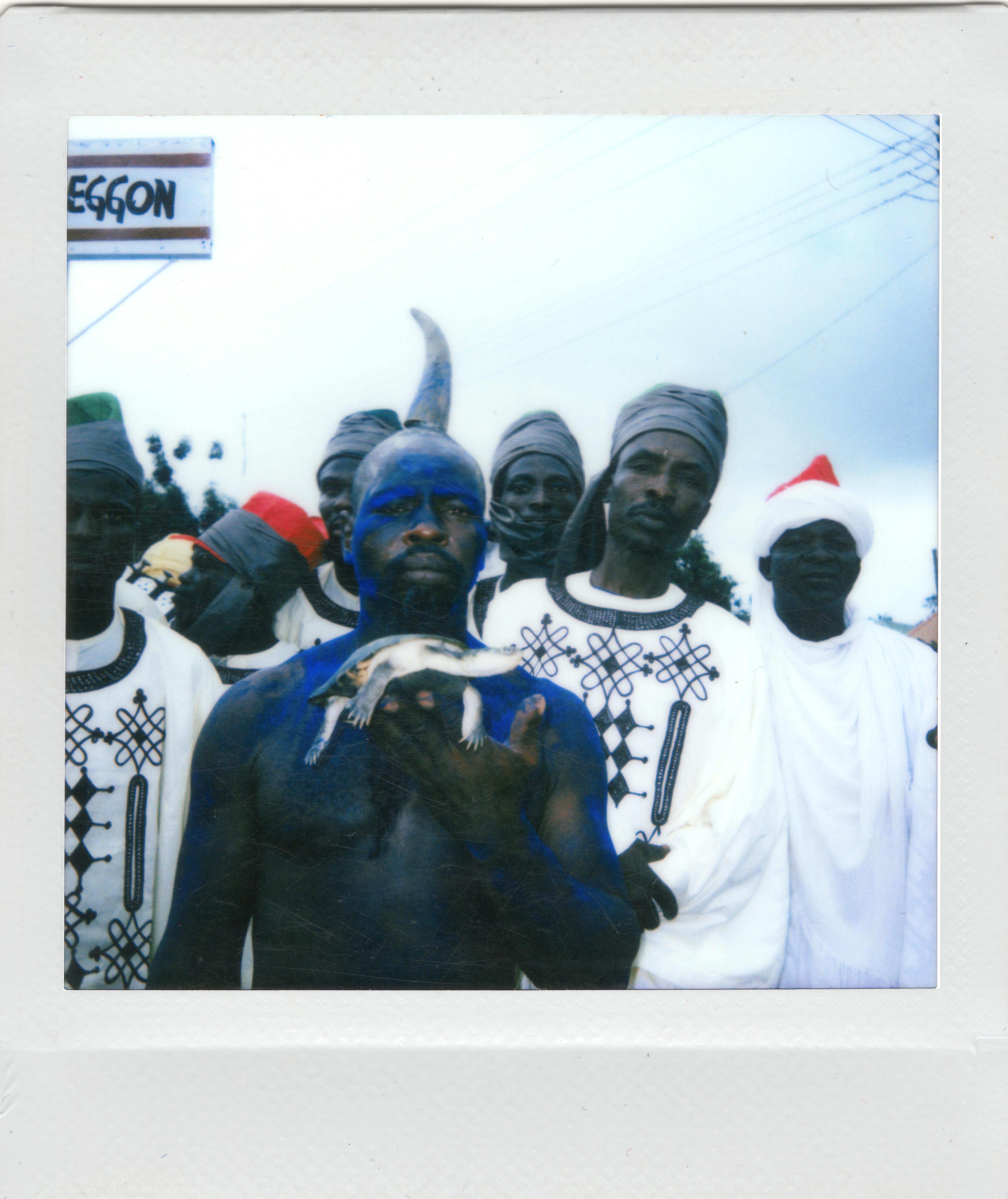 A group of men in traditional attire, with one painted in blue, holding a tortoise.