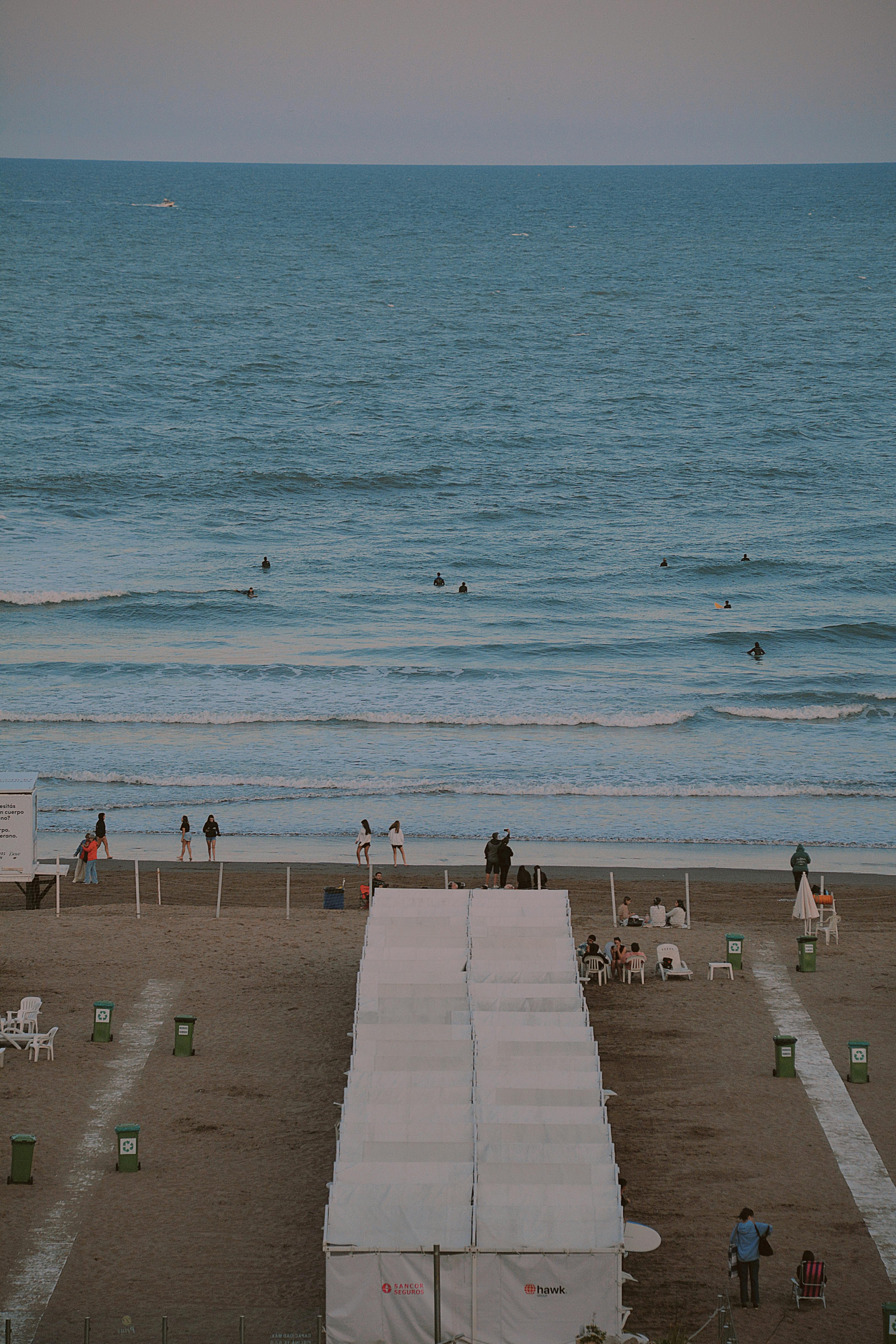 A serene beach scene featuring white tents, people walking, and ocean waves crashing on the shore.