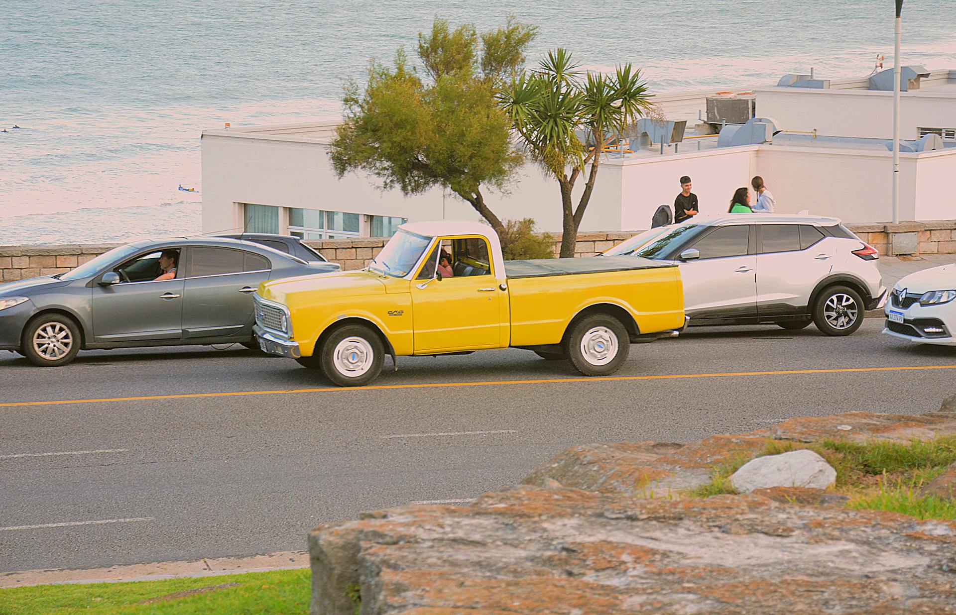 Yellow vintage truck parked by the ocean on a sunny day.