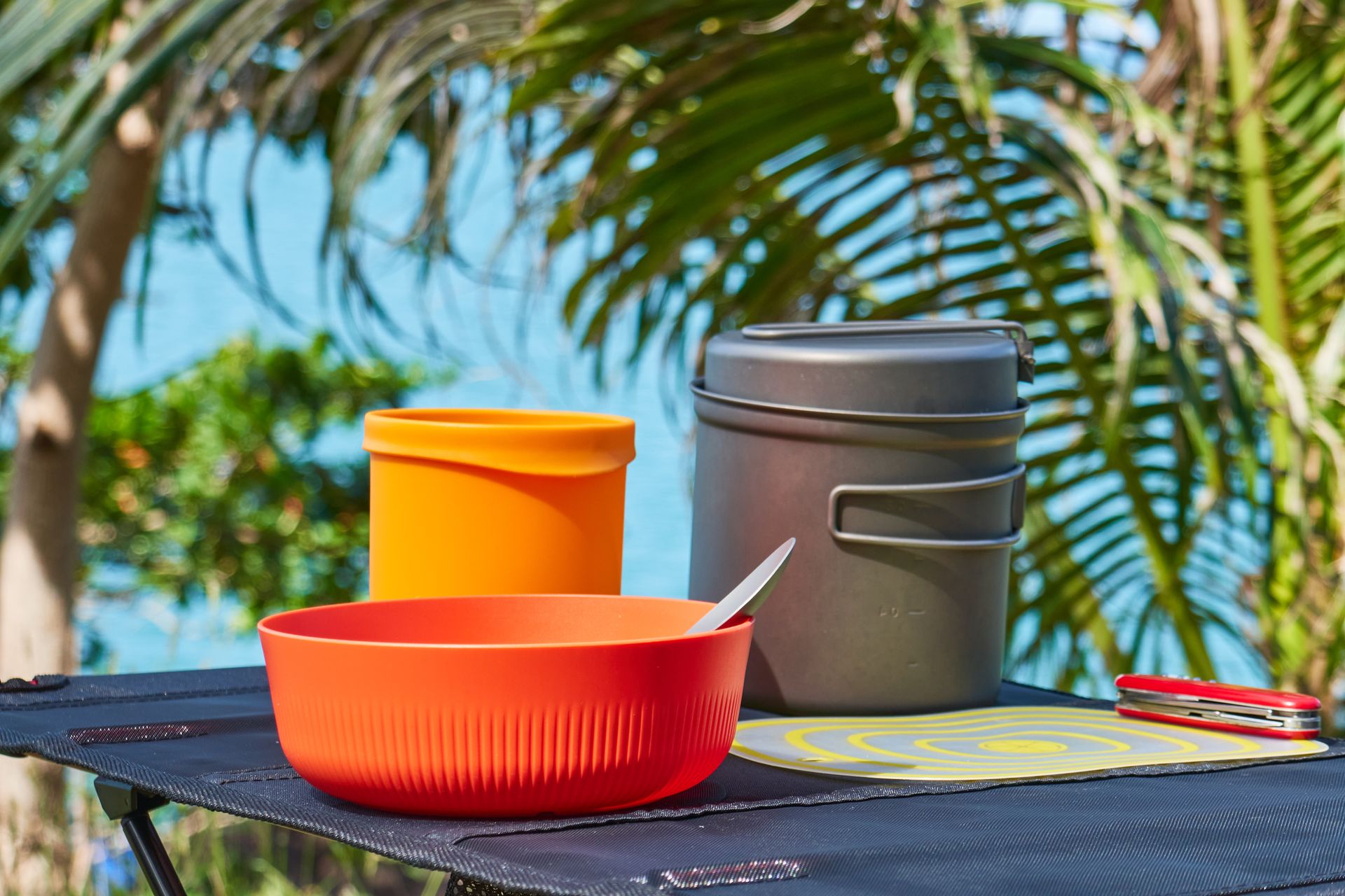 Bright camping cookware set on table with tropical backdrop, Trat, Thailand.