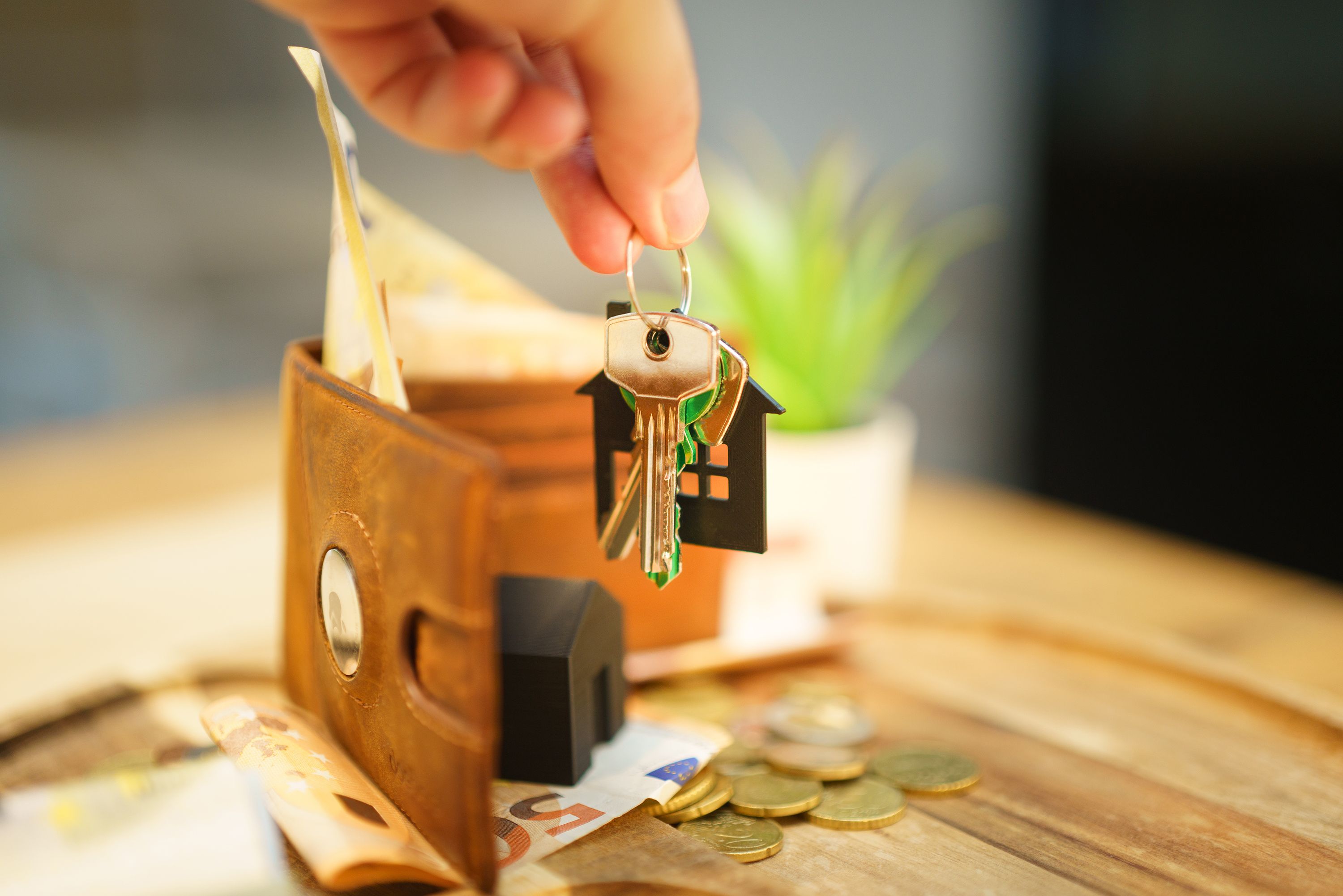 Gratis Primer plano de una mano sosteniendo una llave de casa con una billetera y monedas, simbolizando la inversión inmobiliaria. Foto de stock