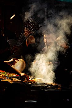Atmospheric night market scene with chefs grilling kebabs amidst smoke.