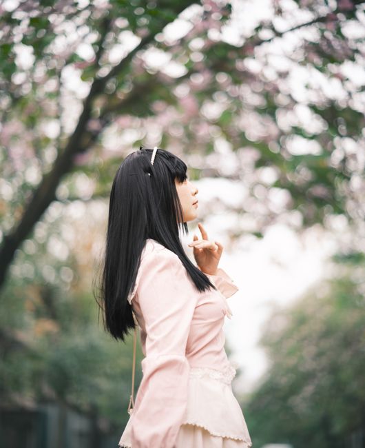 Profile of a woman enjoying cherry blossoms in a serene outdoor setting.