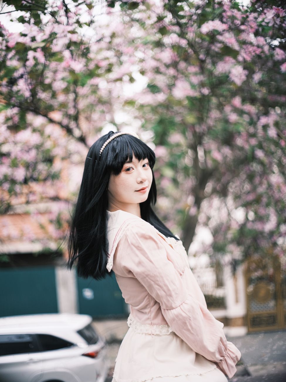 A woman in a pink dress stands among cherry blossoms, exuding a peaceful springtime vibe.