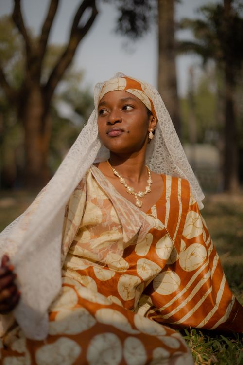 Free An African woman in traditional attire sitting outdoors, radiating grace and cultural beauty. Stock Photo