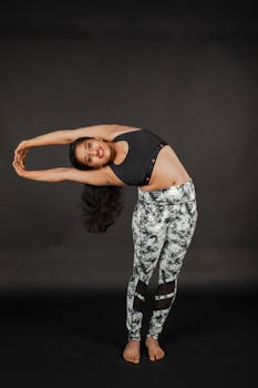 South Asian woman practicing a side stretch yoga pose on a dark background.