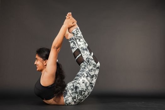 A woman in athletic attire performs the bow pose during a yoga session.
