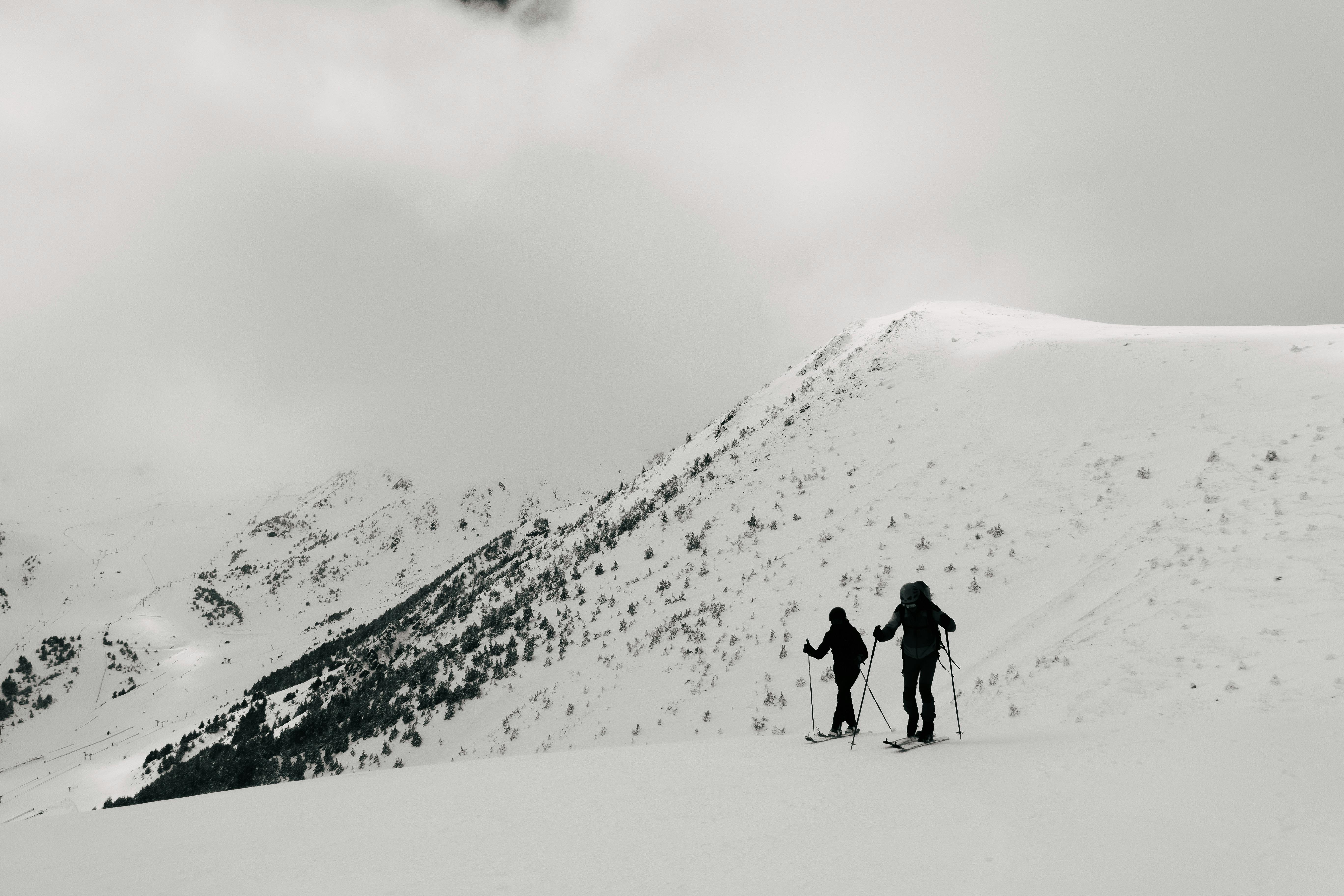 Two skiers hiking through snow-covered mountains under cloudy skies.
