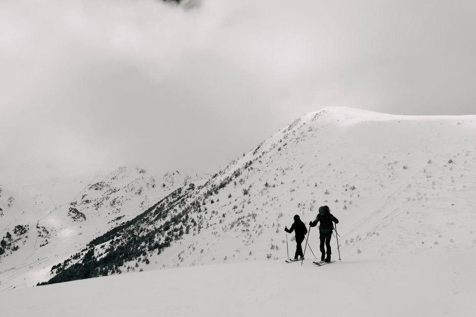 Two skiers hiking through snow-covered mountains under cloudy skies.
