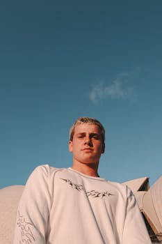 Young adult male posing at Sydney Opera House under bright blue sky, conveying a modern architectural vibe.