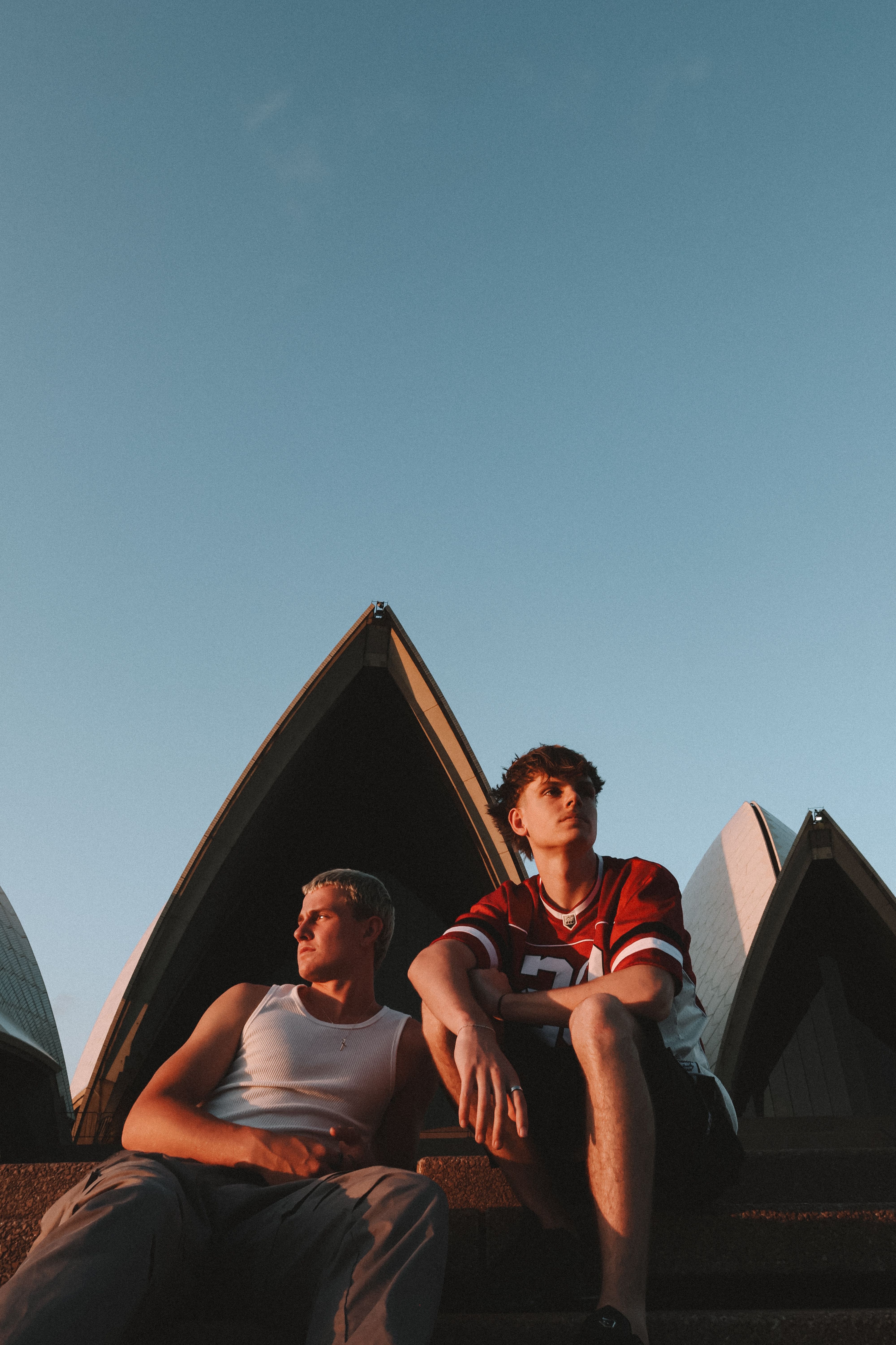 Two young adults sitting near Sydney Opera House, capturing the city vibe at sunset.