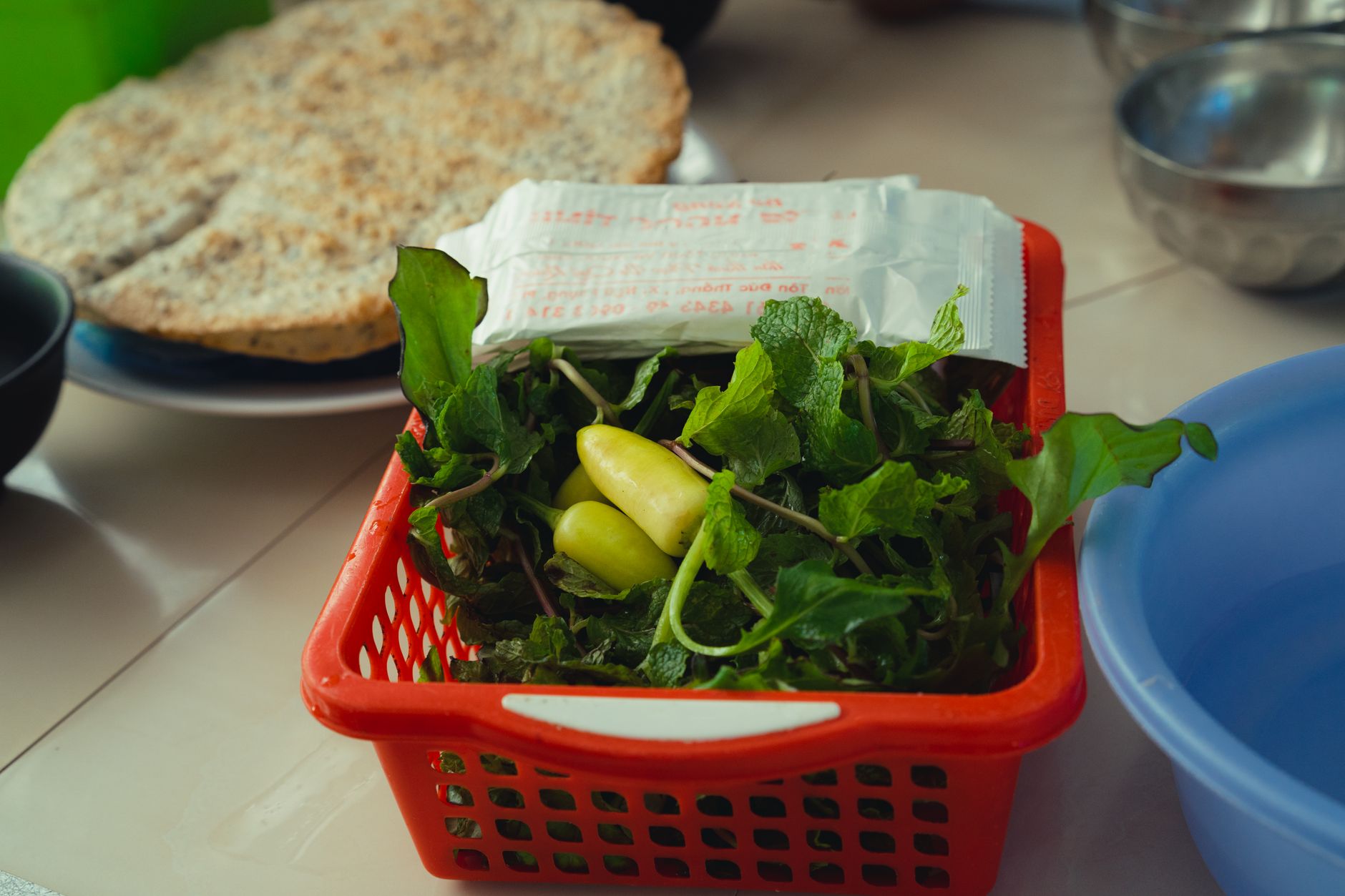 Red basket containing fresh Vietnamese herbs and chili peppers, perfect for culinary use.