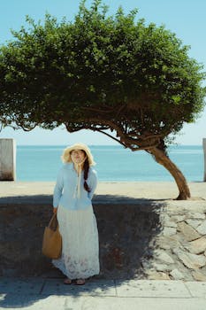 A woman in a sun hat stands near a tree by the ocean in Bình Thuận, Vietnam.