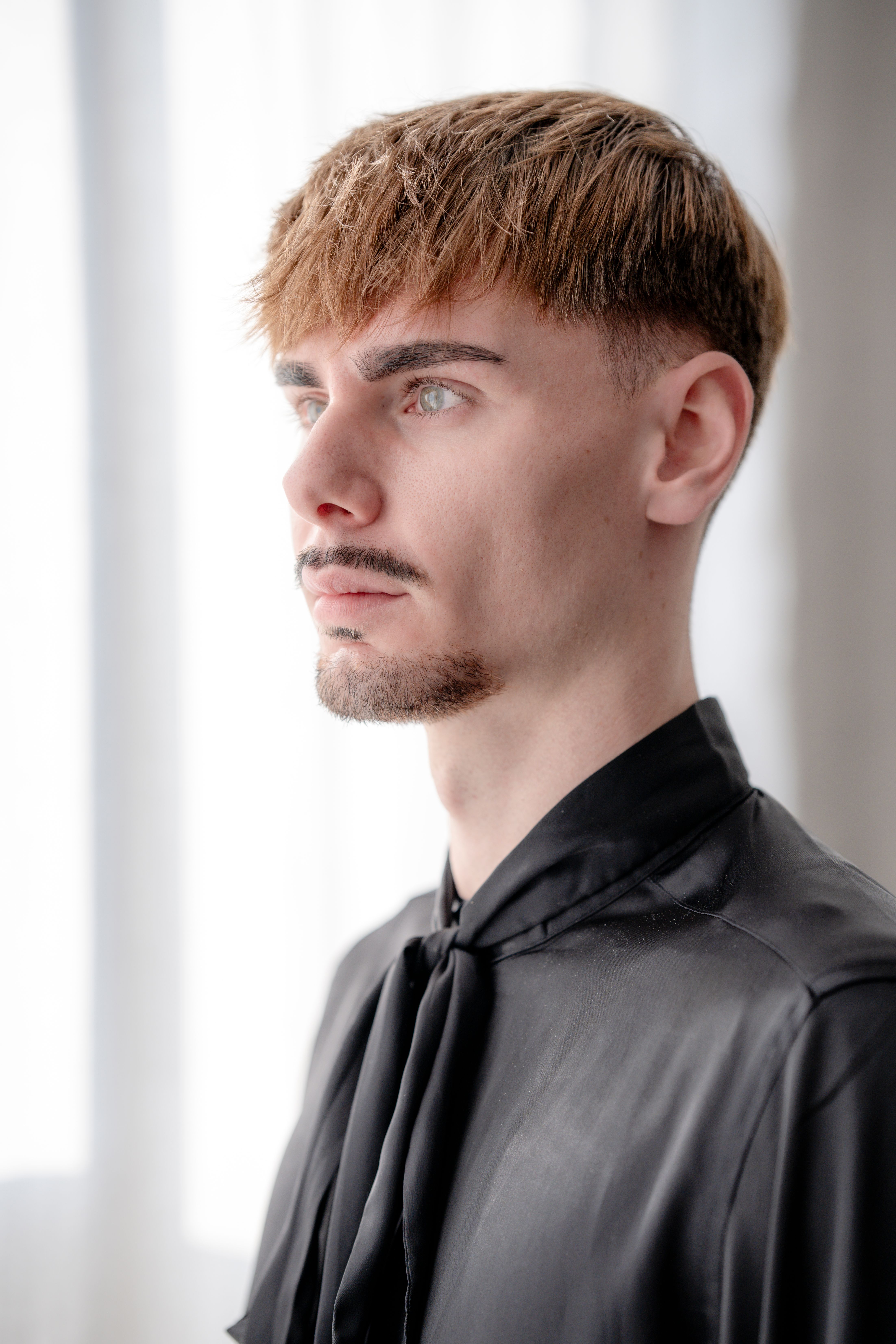 Profile portrait of a young man with short hair, wearing a black shirt indoors.