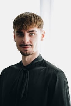 Elegant portrait of a young man in a black shirt against a bright background.