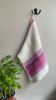Elegant crochet kitchen towel with pink and white stripes next to a fresh basil plant. Perfect for a country kitchen.