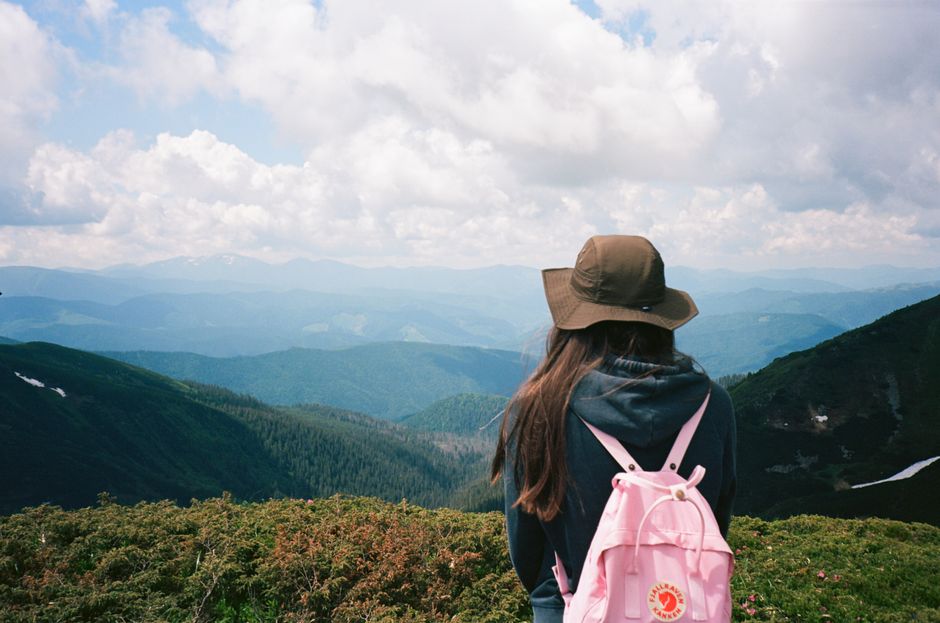 A young woman with a backpack enjoys a stunning mountain view during summer.