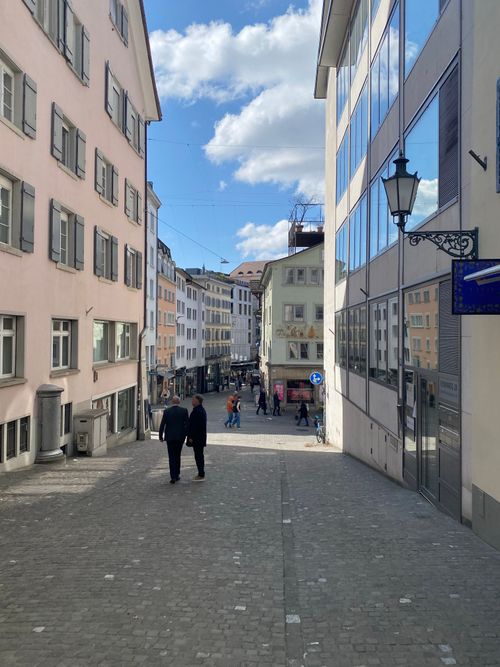 Free A cozy European street, featuring classic architecture and people strolling under a blue sky. Stock Photo
