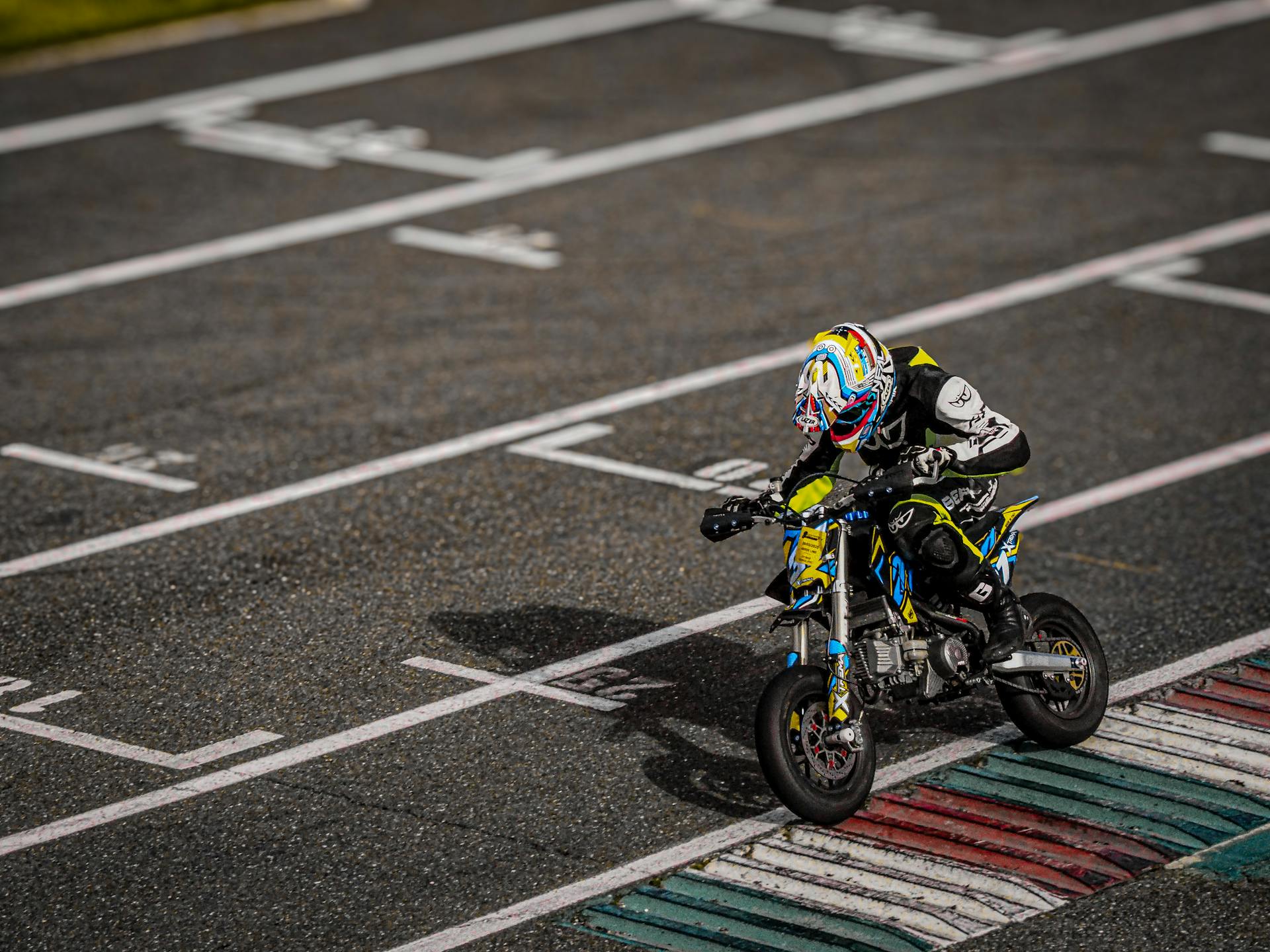Mini motorbike racer accelerates past start line on an empty circuit track.