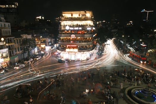 Long exposure of a lively city intersection at night with light trails and bustling activity.