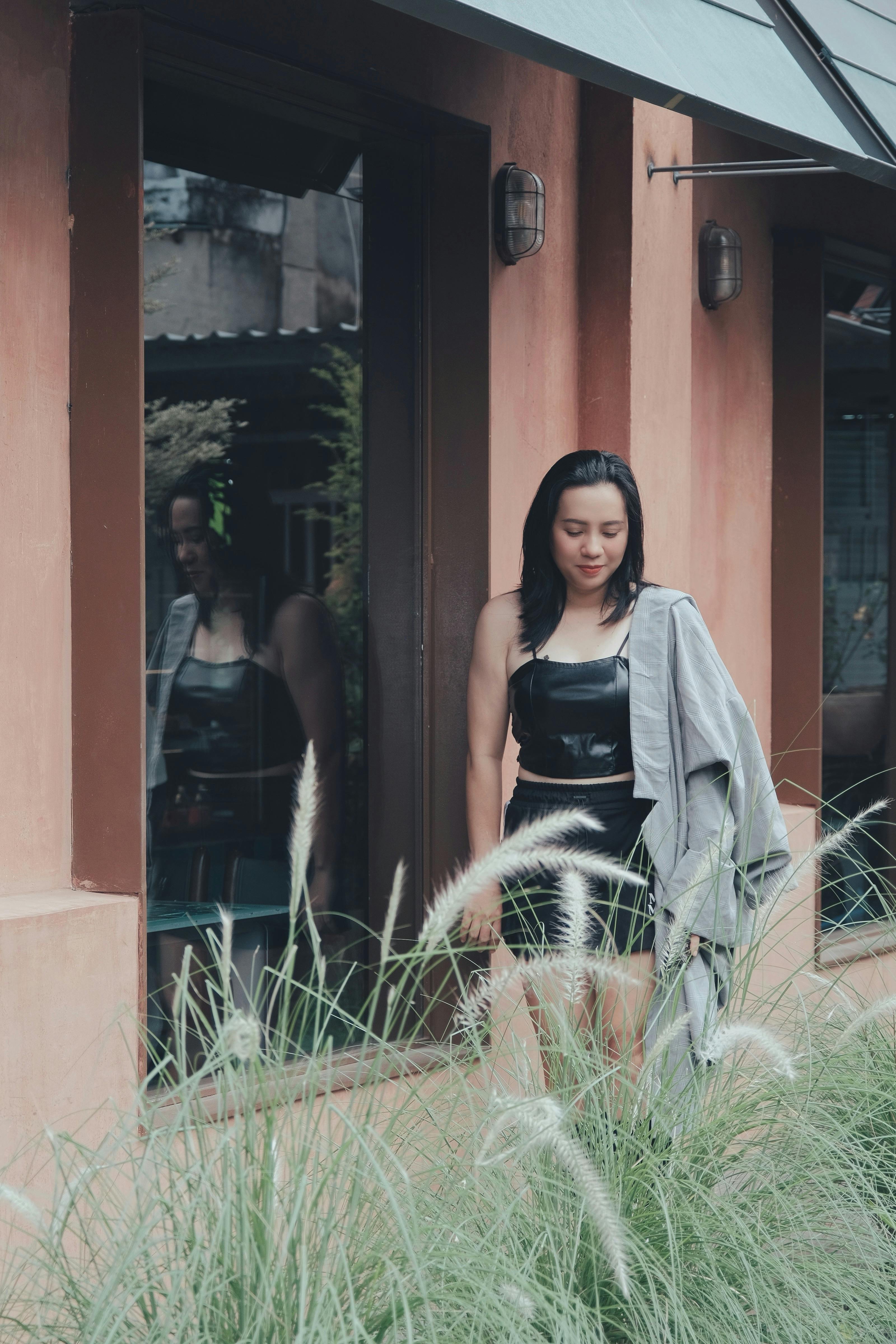Fashionable young woman in leather crop top and shorts walking outside a modern building on a summer day.