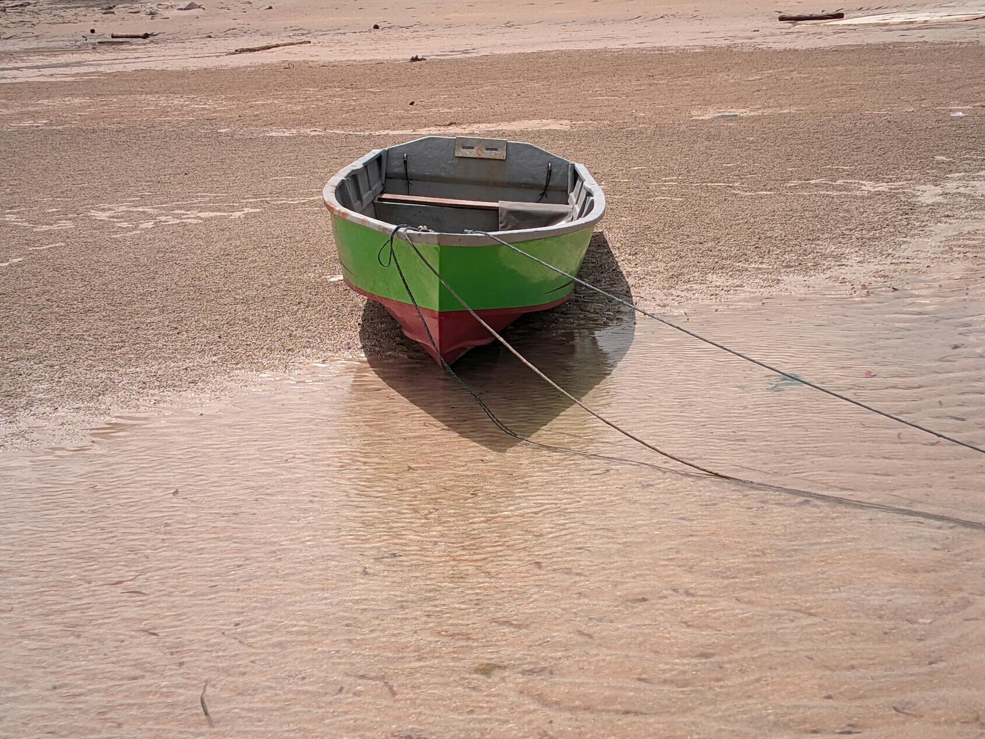A small boat sits stranded on a sandy beach during low tide on the Riau Islands, Indonesia.