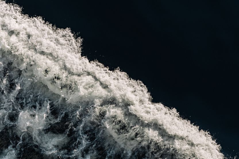 Aerial view of a breaking wave against dark open water — photo by Anton Massalov on Pexels