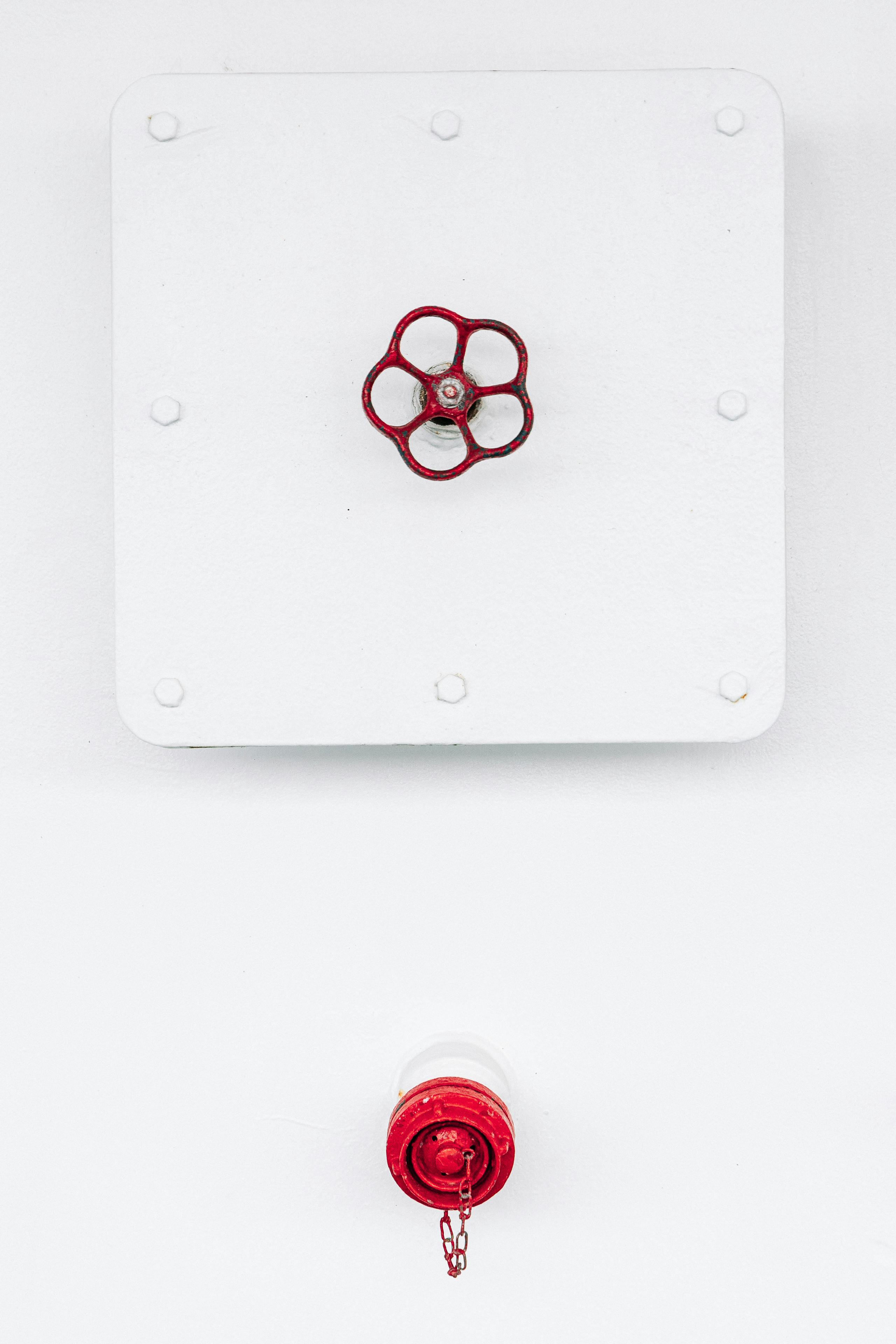 бесплатная Красный промышленный клапан и сигнализация на белой стене, передающие простоту и контраст. Стоковое фото