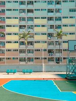 Vibrant urban basketball court in front of pastel buildings with palm trees in Kowloon, Hong Kong.