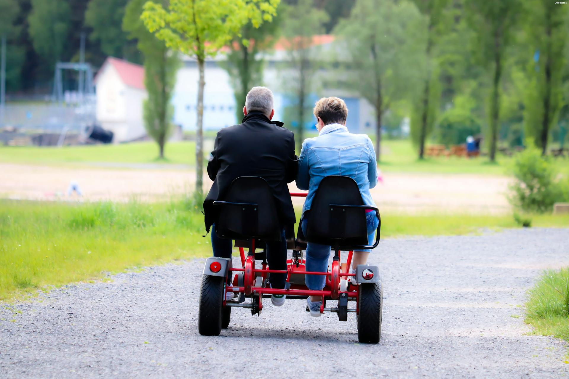 A couple enjoys a leisurely ride on a tandem bike through a lush park.