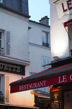 Cozy Montmartre street view showcasing classic Parisian architecture and restaurant signs at twilight.